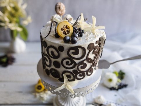 Na zdjęciu widać tort o smaku czekoladowym, udekorowany śmietaną i efektownymi czekoladowymi ornamentami.