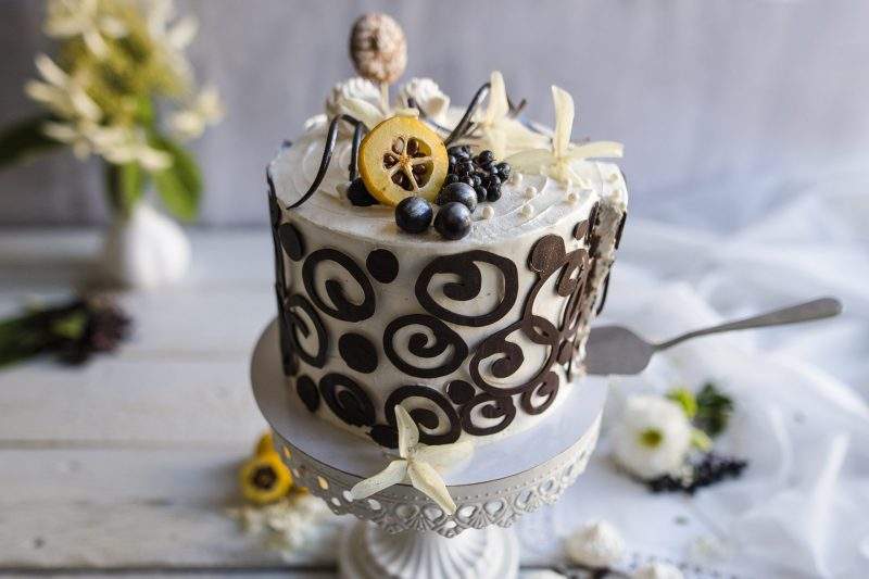 Na zdjęciu widać tort o smaku czekoladowym, udekorowany śmietaną i efektownymi czekoladowymi ornamentami.